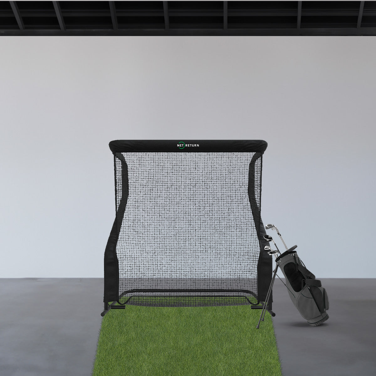 Golf hitting net set up indoors on a patch of artificial grass next to a golf bag.