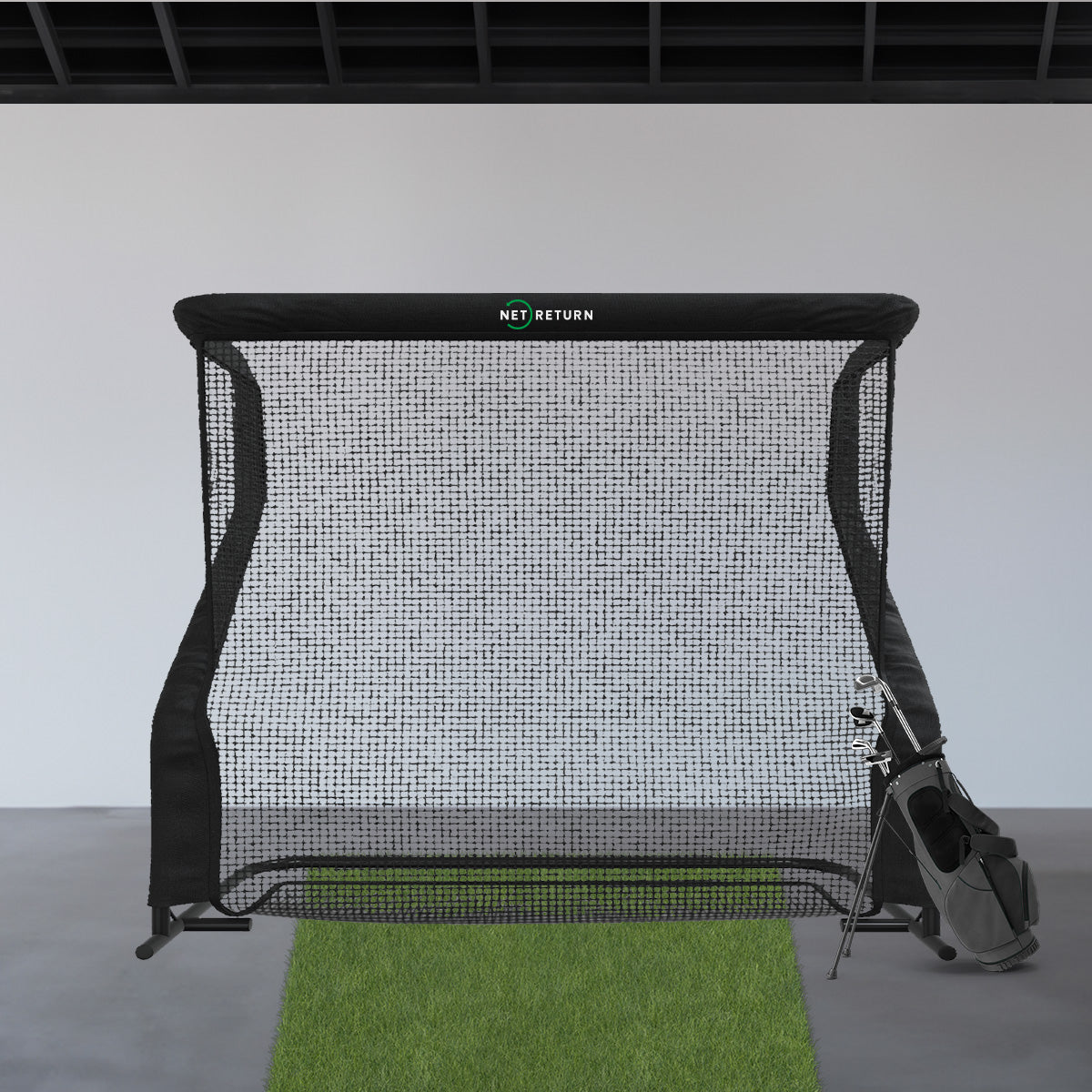 A golf practice net is set up indoors with a green mat and a golf bag nearby.