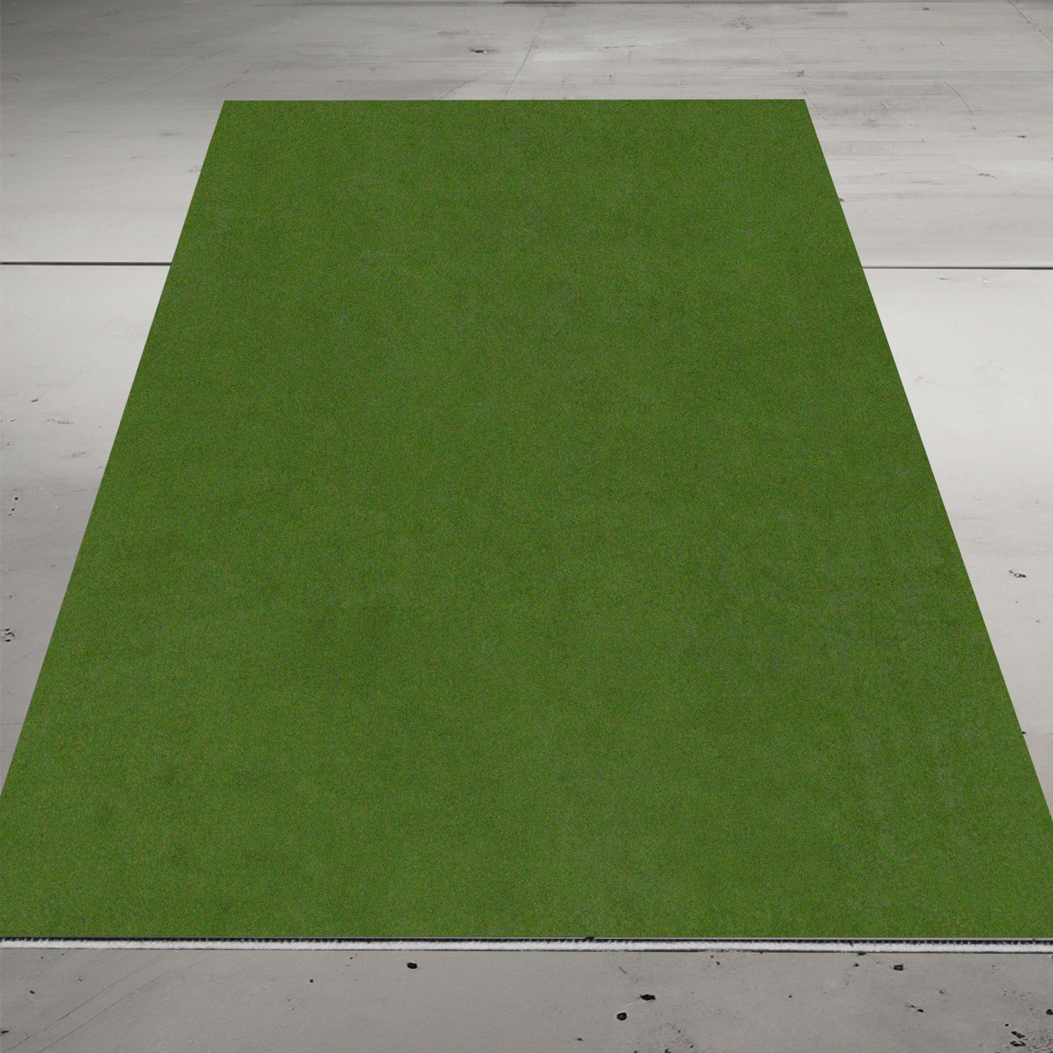 A rectangular patch of green artificial grass is laid on a gray concrete floor.