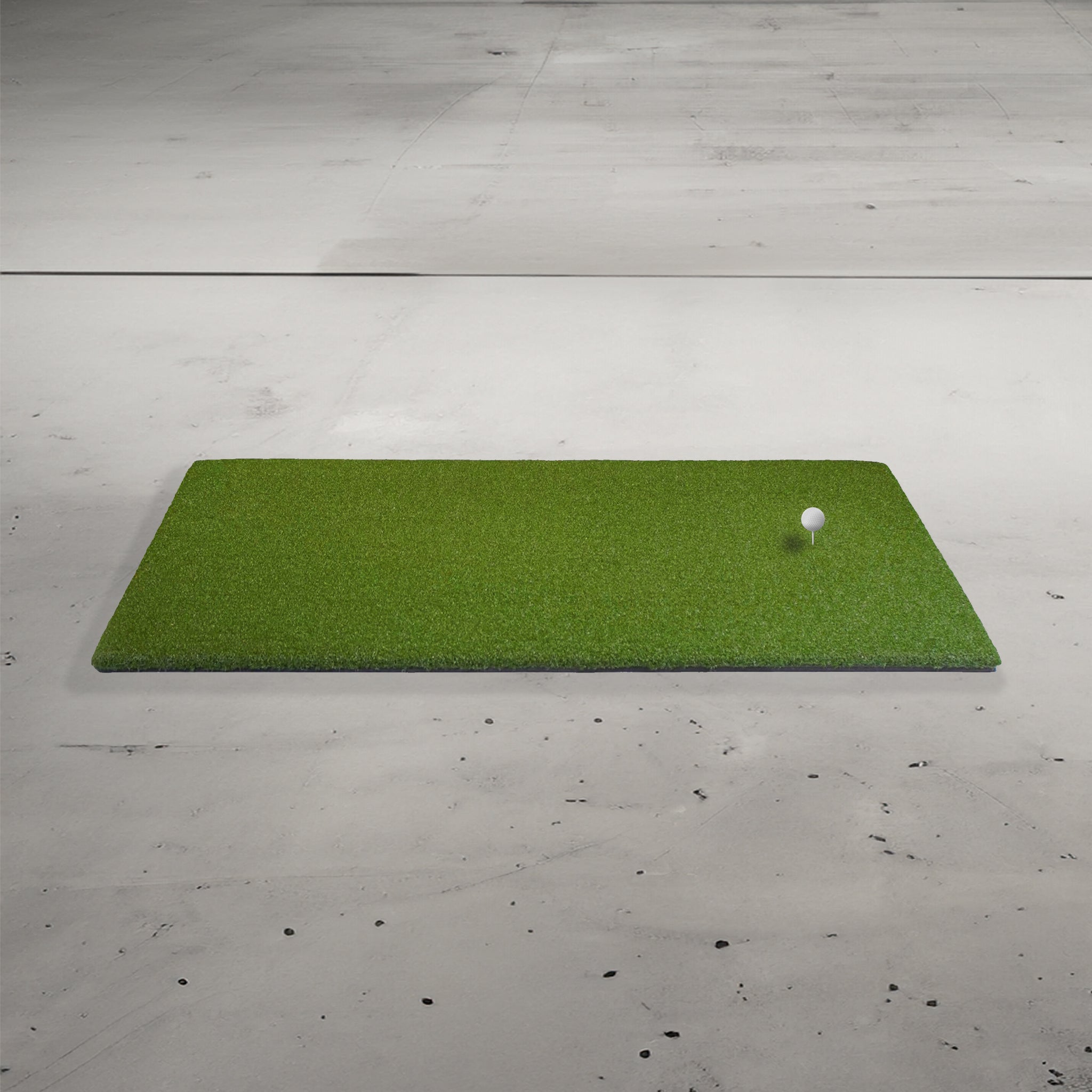 A green artificial turf mat on a concrete floor with a golf ball on a tee.
