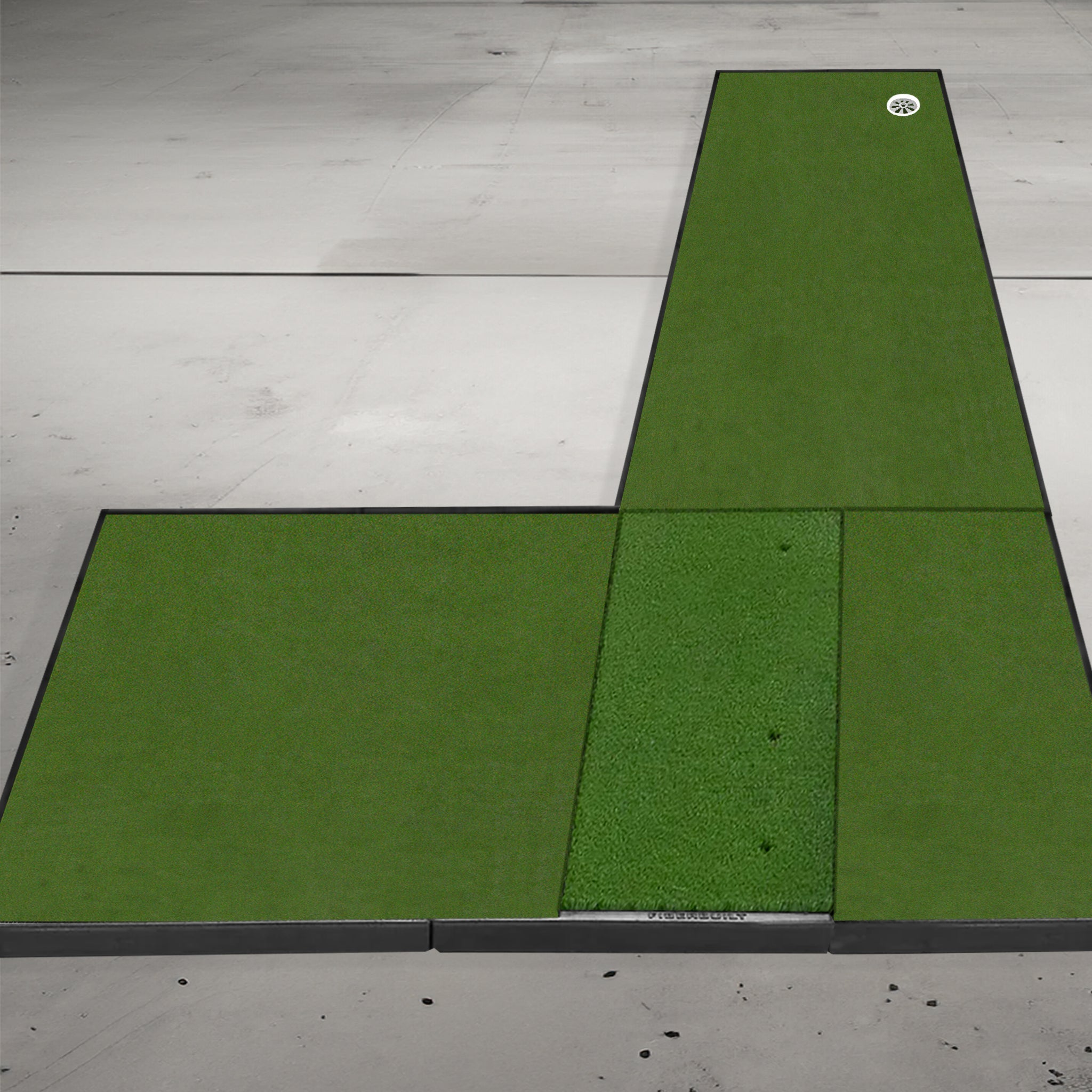 Golf putting mat setup on a concrete floor featuring three green sections, one with a golf ball near the edge.