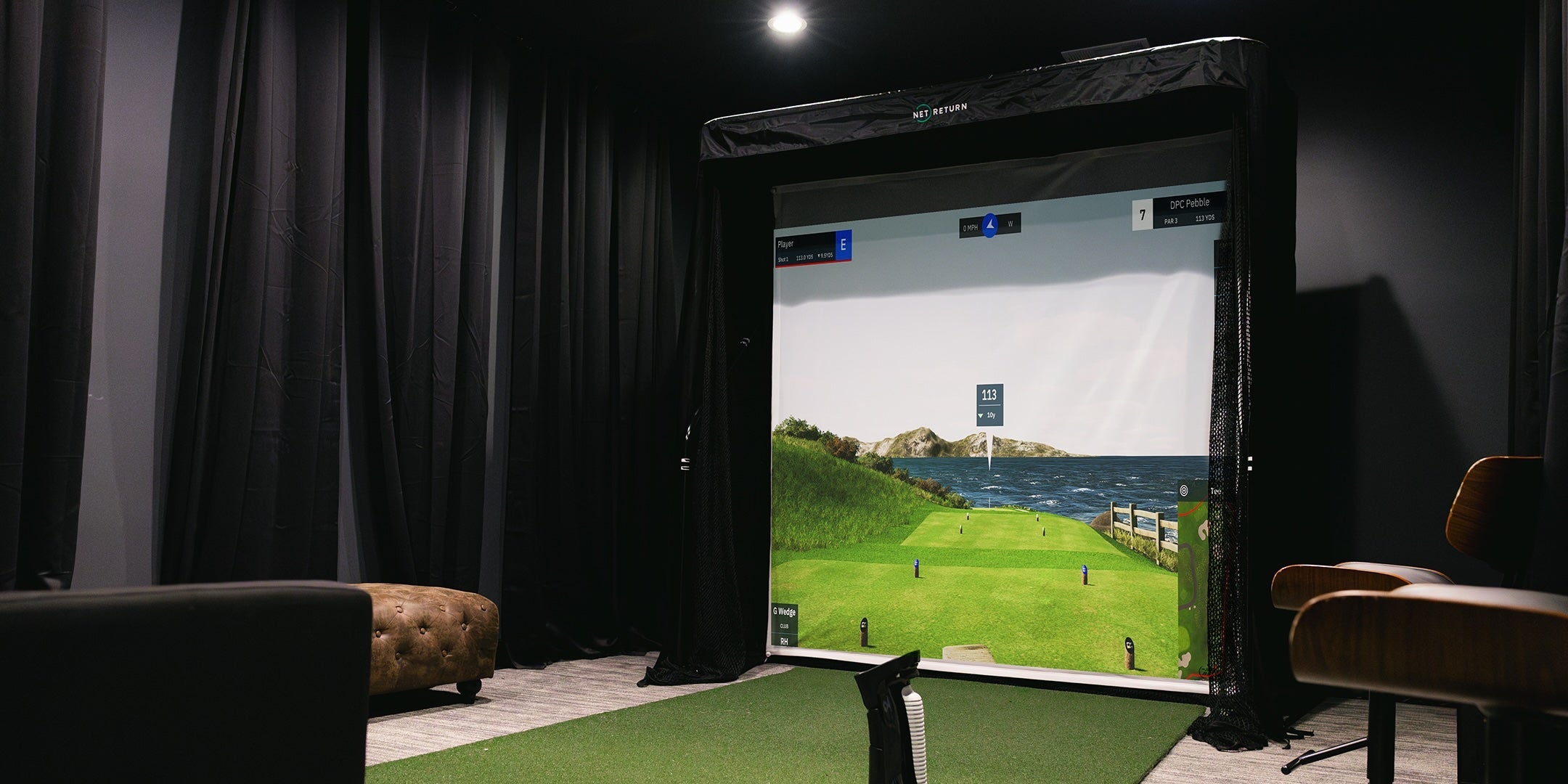 A golf simulator setup in a dimly lit room with a large screen displaying a golf course scene.